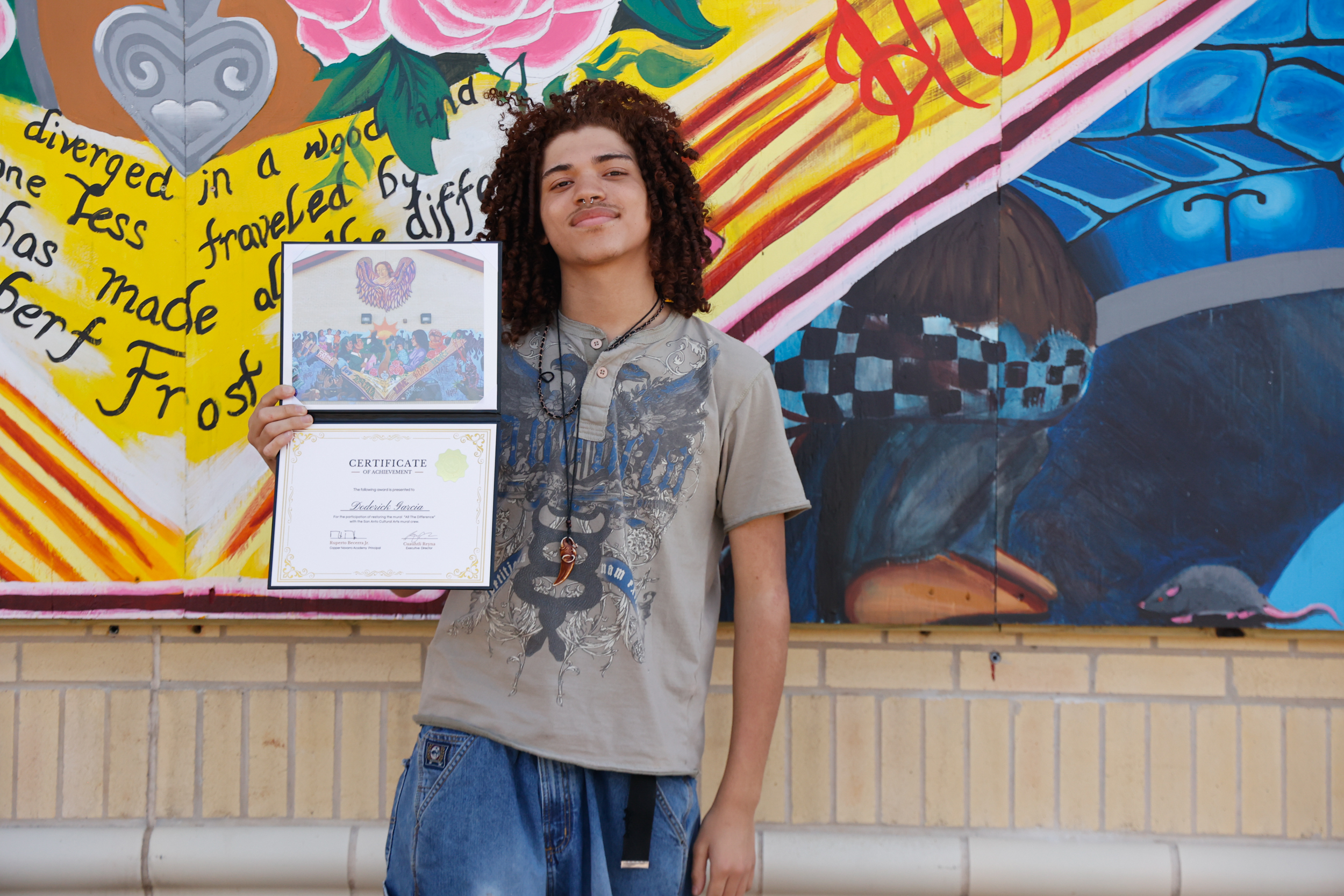 Male student stands in front of mural with certificate