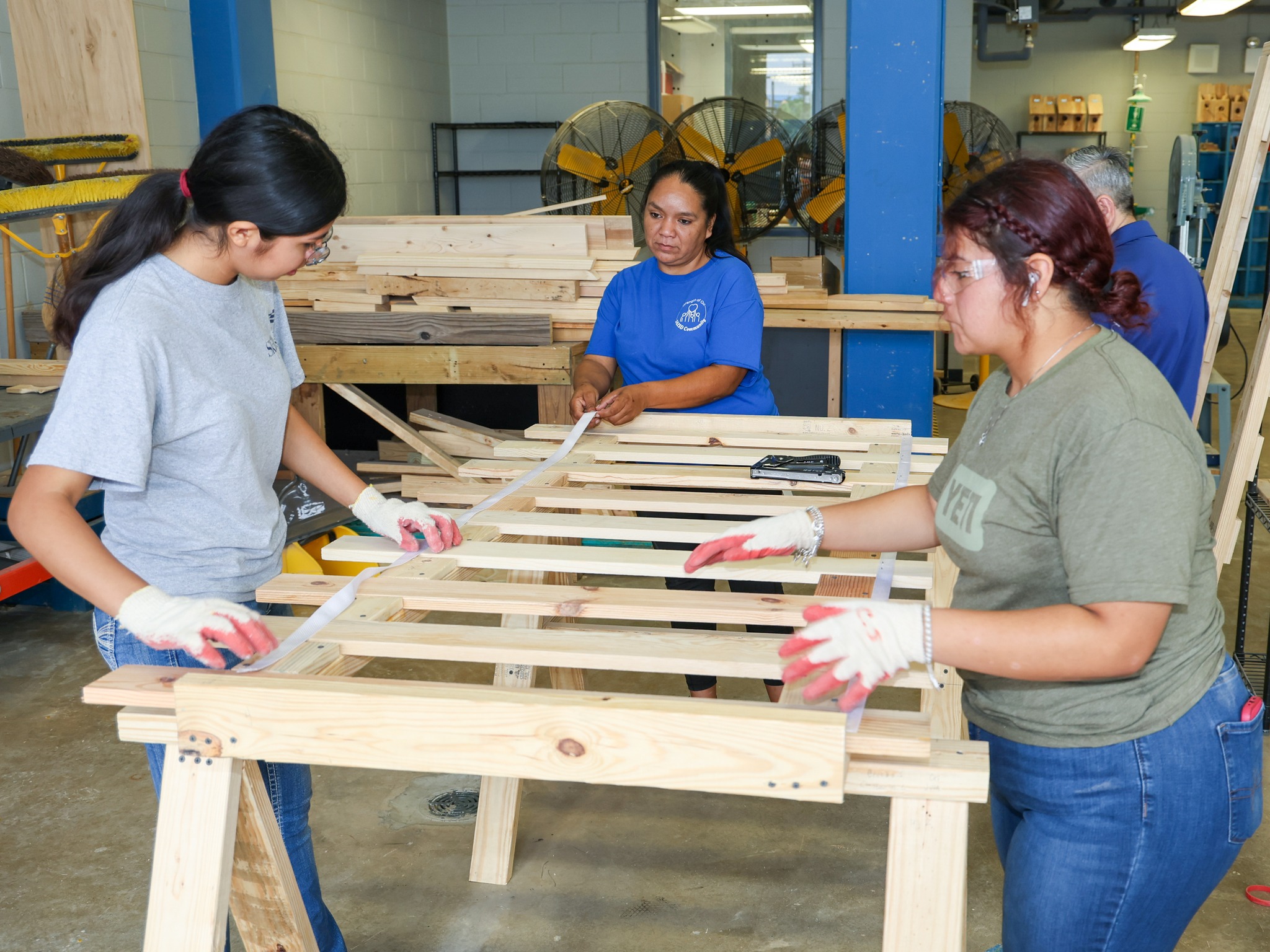Two female construction students build bed frame with Trustee Torres