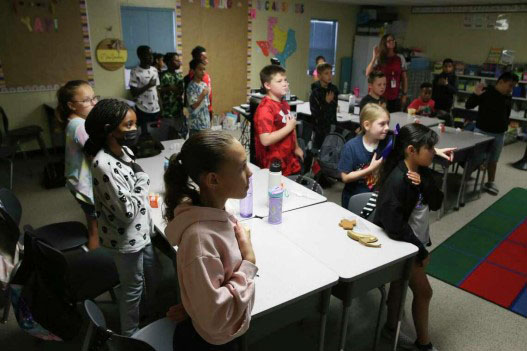 Students in a classroom saying the Pledge of Allegiance