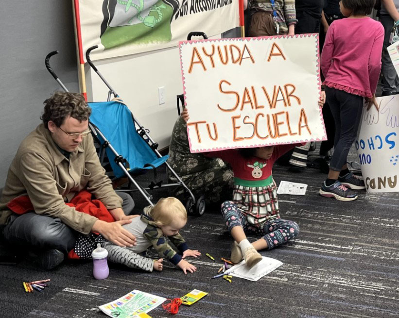 Family sits on floor with children playing during SAISD board meeting